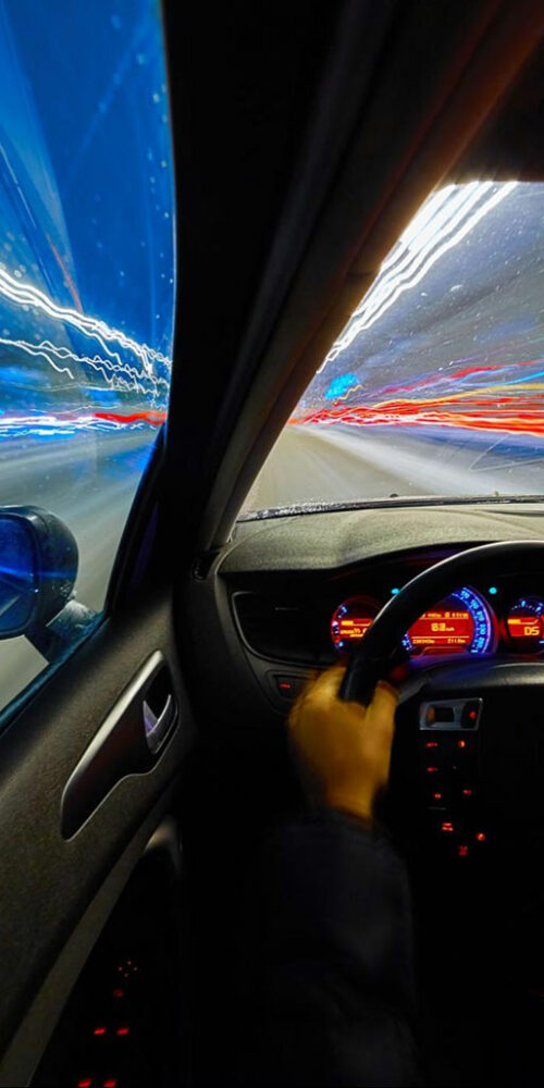Driver's perspective of a high-speed night drive with motion blur from the city lights and traffic.